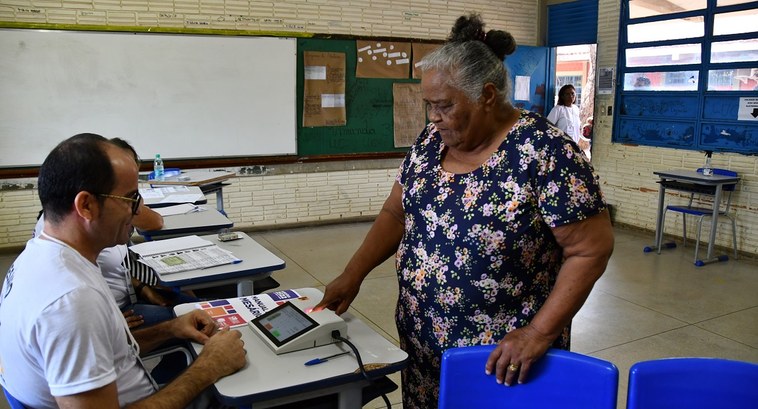 Mulher colocando o dedo no leitor biométrico da urna eletrônica, se preparando para votar.