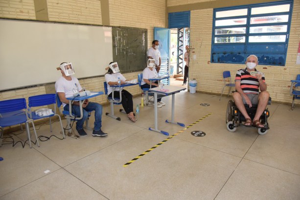 Foto colorida de seção eleitoral com quatro mesários e eleitor cadeirante