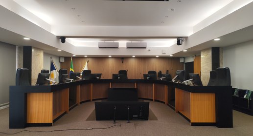 A imagem mostra o interior do plenário do TRE-TO, com aparência moderna e organizada. No centro,...