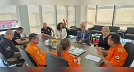 A imagem registra uma reunião institucional em um escritório amplo e iluminado por luz natural, ...