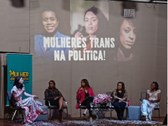 foto colorida da roda de conversa, com 5 mulheres sentadas lado a lado e com uma mesa com flores...