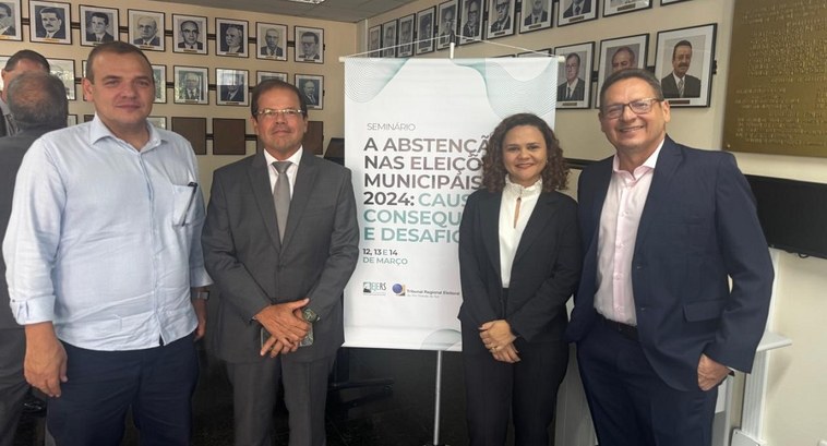 TRE-TO participa de evento que analisa a abstenção nas Eleições Municipais de 2024 A imagem mostra quatro pessoas posando para uma foto ao lado de um banner do seminário "A Absten...