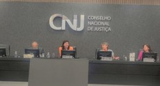 A imagem mostra uma reunião no CNJ, com quatro pessoas sentadas à mesa central, aparentemente di...