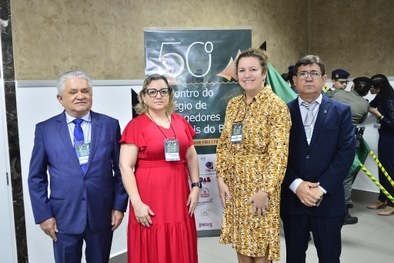 Imagem colorida de representantes do TRE-TO em frente ao banner do 50º Encontro do Colégio de Co...