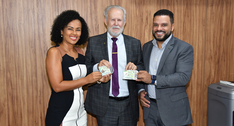 A imagem mostra o desembargador, a diretora e o superintendente, lado a lado, sorrindo e seguran...